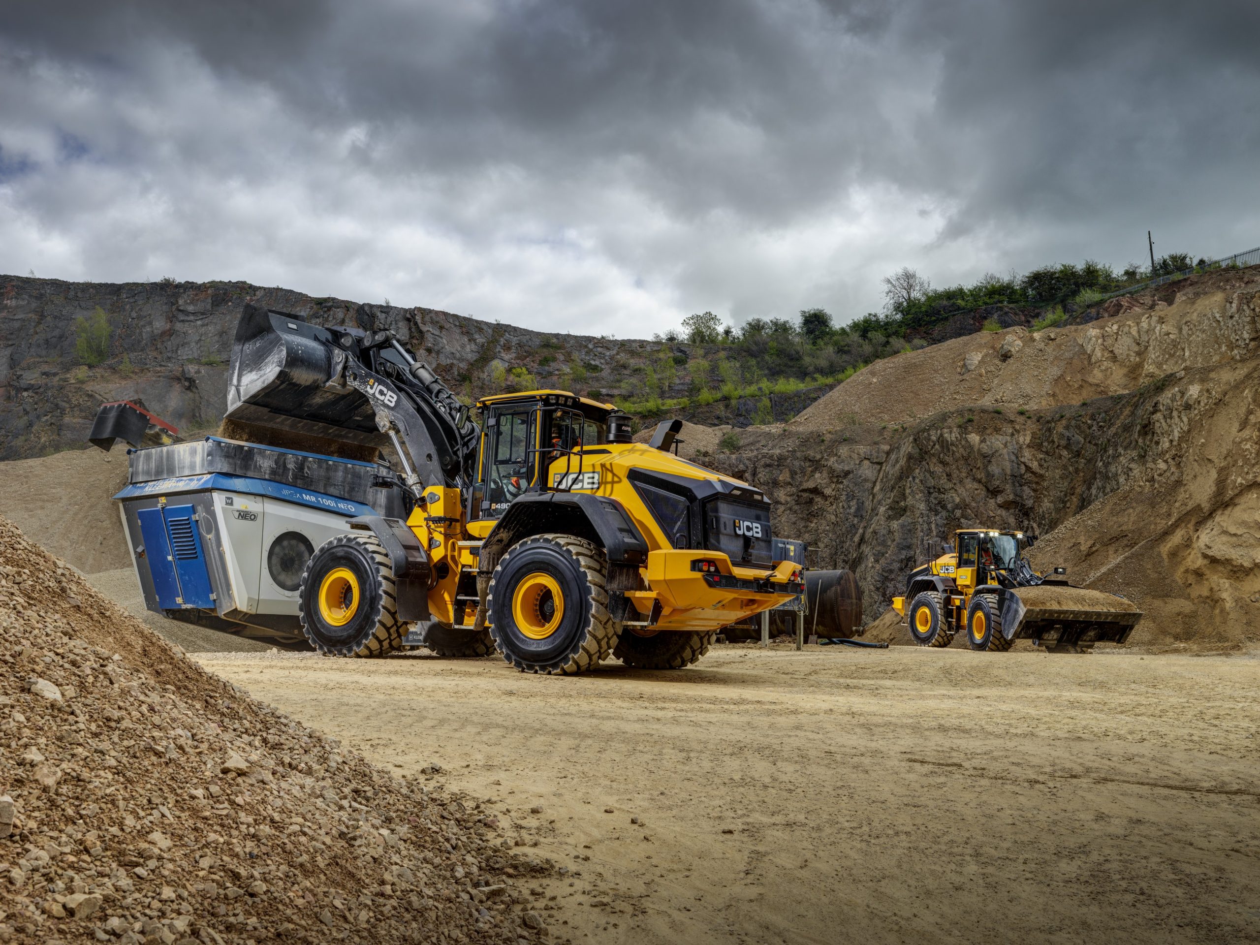 La nuova pala gommata JCB 490 mentre carica con precisione la tramoggia di un frantoio mobile all'interno di una cava, massimizzando l'efficienza del ciclo di lavoro.