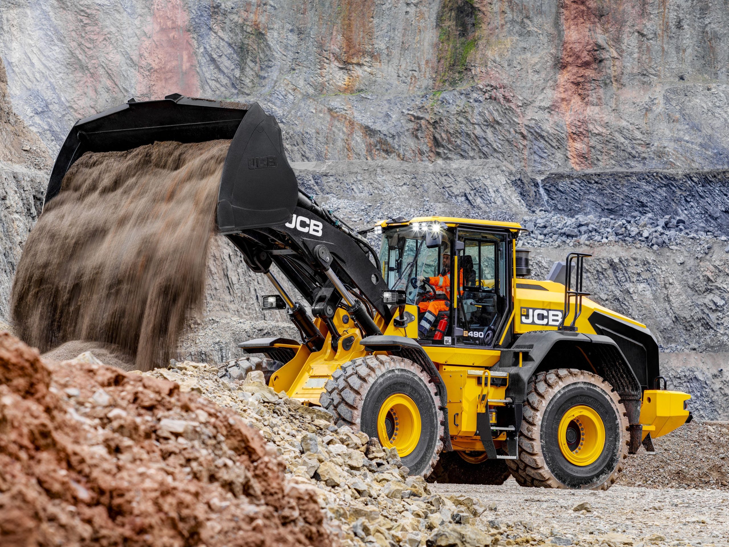 La pala gommata JCB 490 durante lo scarico di materiale in cava, con il braccio sollevato che mette in mostra il nuovo design del cinematismo brevettato.