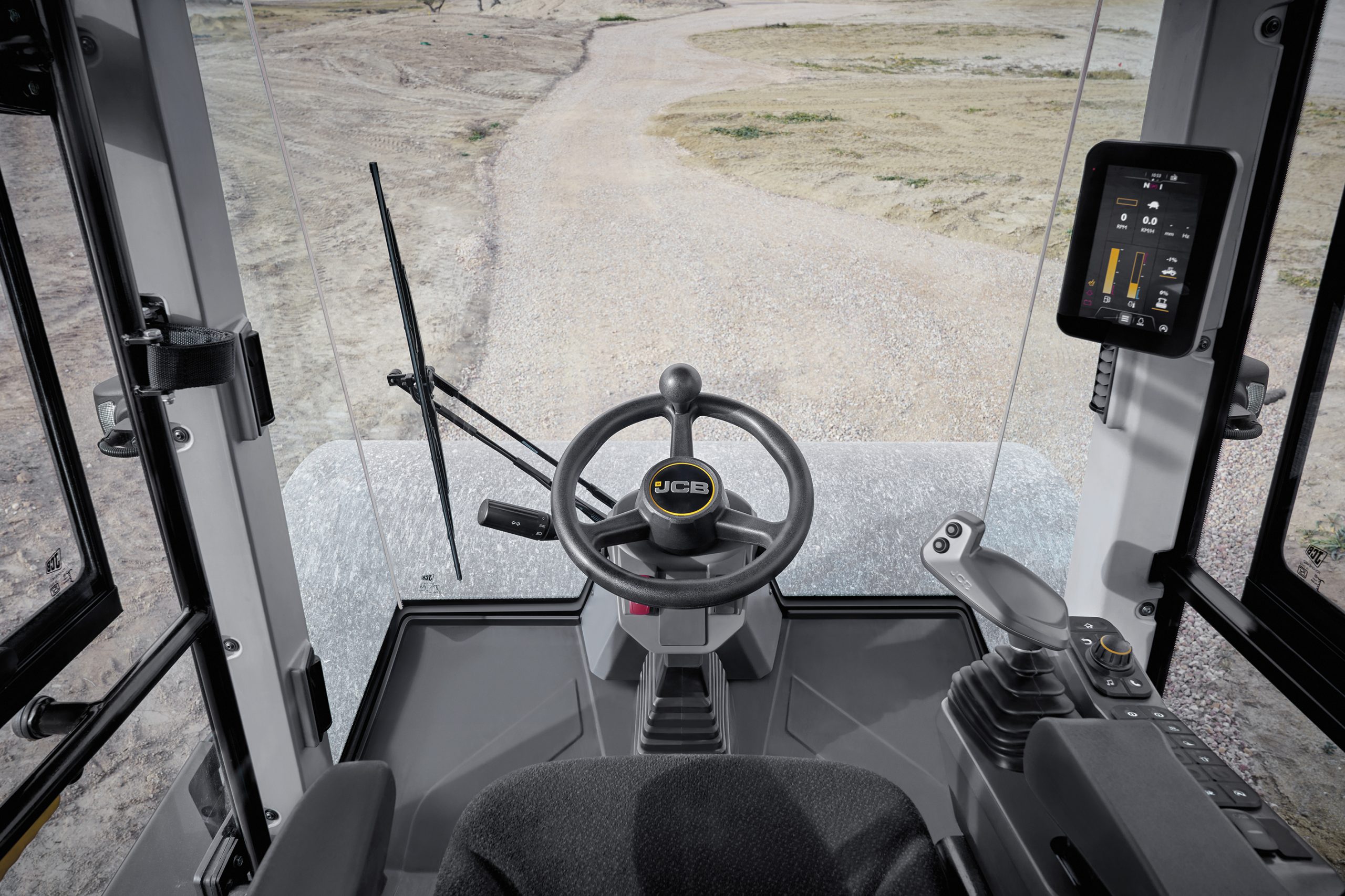 Vista dall'interno della cabina del compattatore JCB VM118D: l'ampia visibilità sul tamburo e sul tracciato si combina a una postazione di guida ergonomica e avanzata.