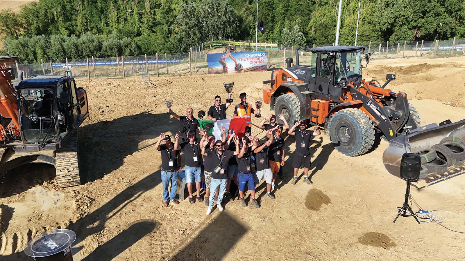 Foto di gruppo per i 13 operatori italiani protagonisti del LANDCROS Operator Challenge a Faenza, festeggiati con le coppe e il tricolore tra i mezzi HITACHI forniti da Scai.