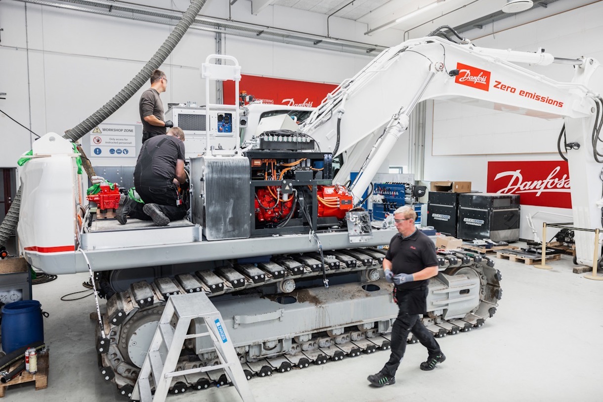 Ingegneri e tecnici al lavoro in officina per la conversione elettrica di un escavatore con tecnologia DANFOSS a zero emissioni.