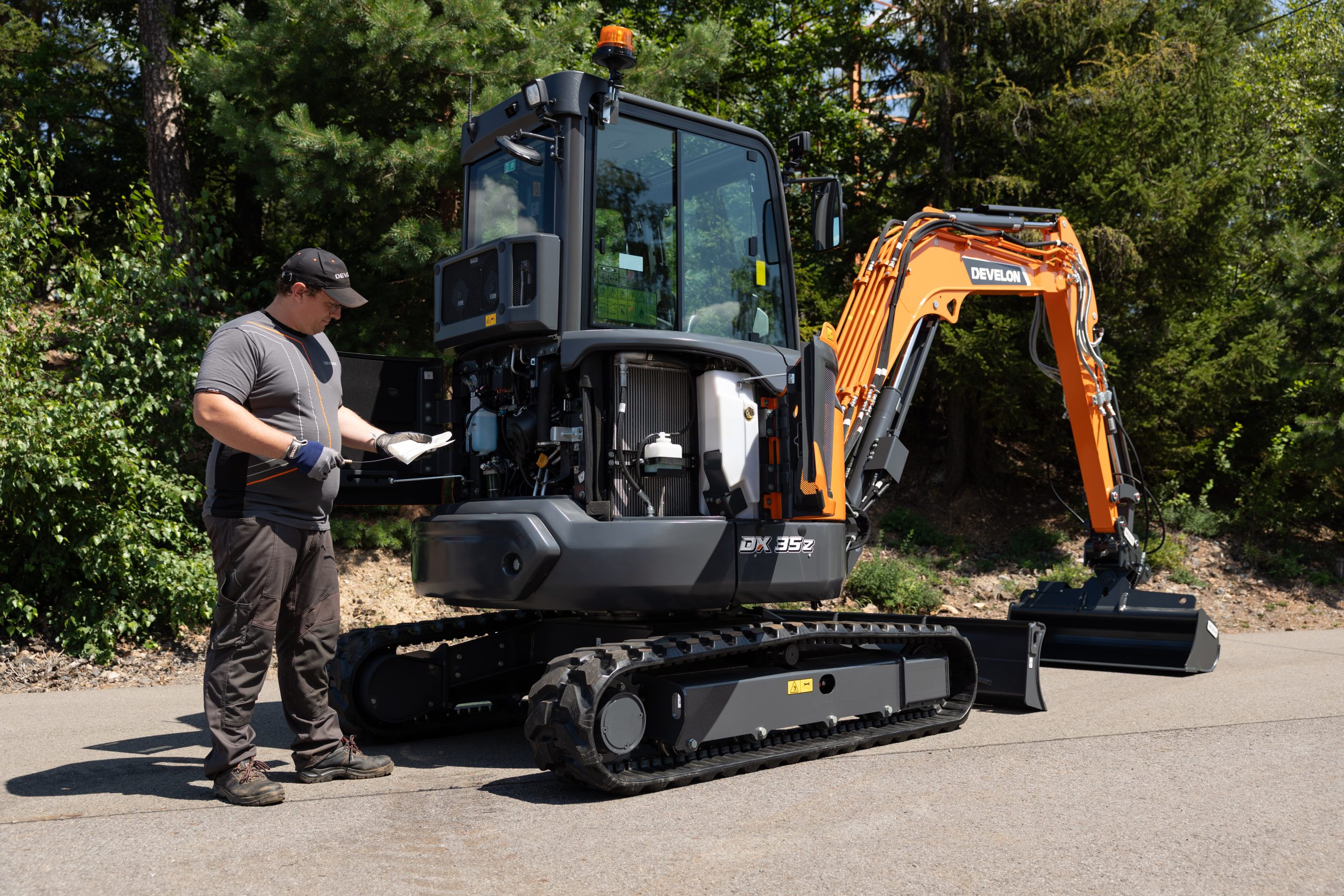 Operazioni di ispezione sul mini escavatore Develon DX35Z-7, progettato con vani ampi per agevolare il controllo dei livelli e i regolari interventi di servizio.