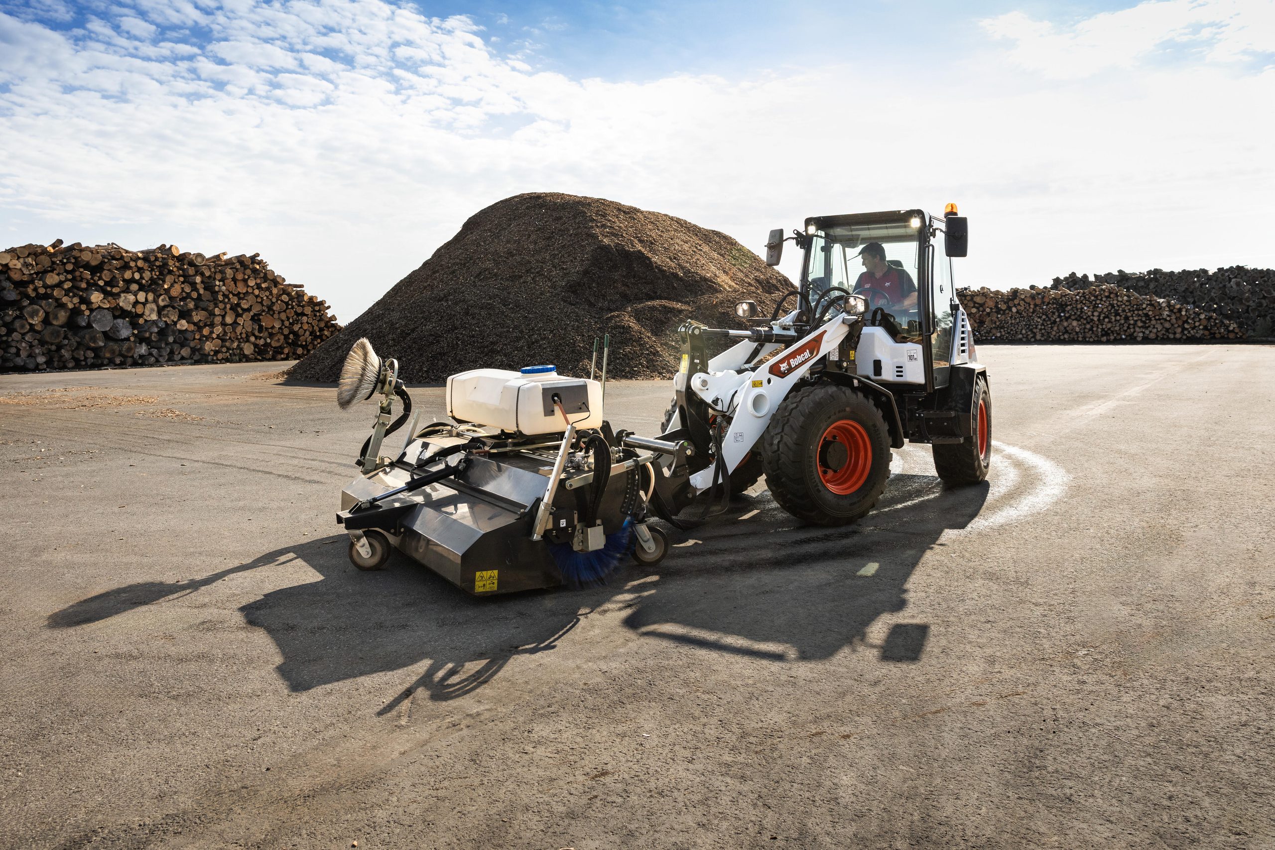La nuova pala gommata compatta Bobcat L100 all'opera con uno spazzolone con benna di raccolta, sfruttando la maggiore potenza idraulica ausiliaria e l'opzione High Flow per le applicazioni più esigenti.