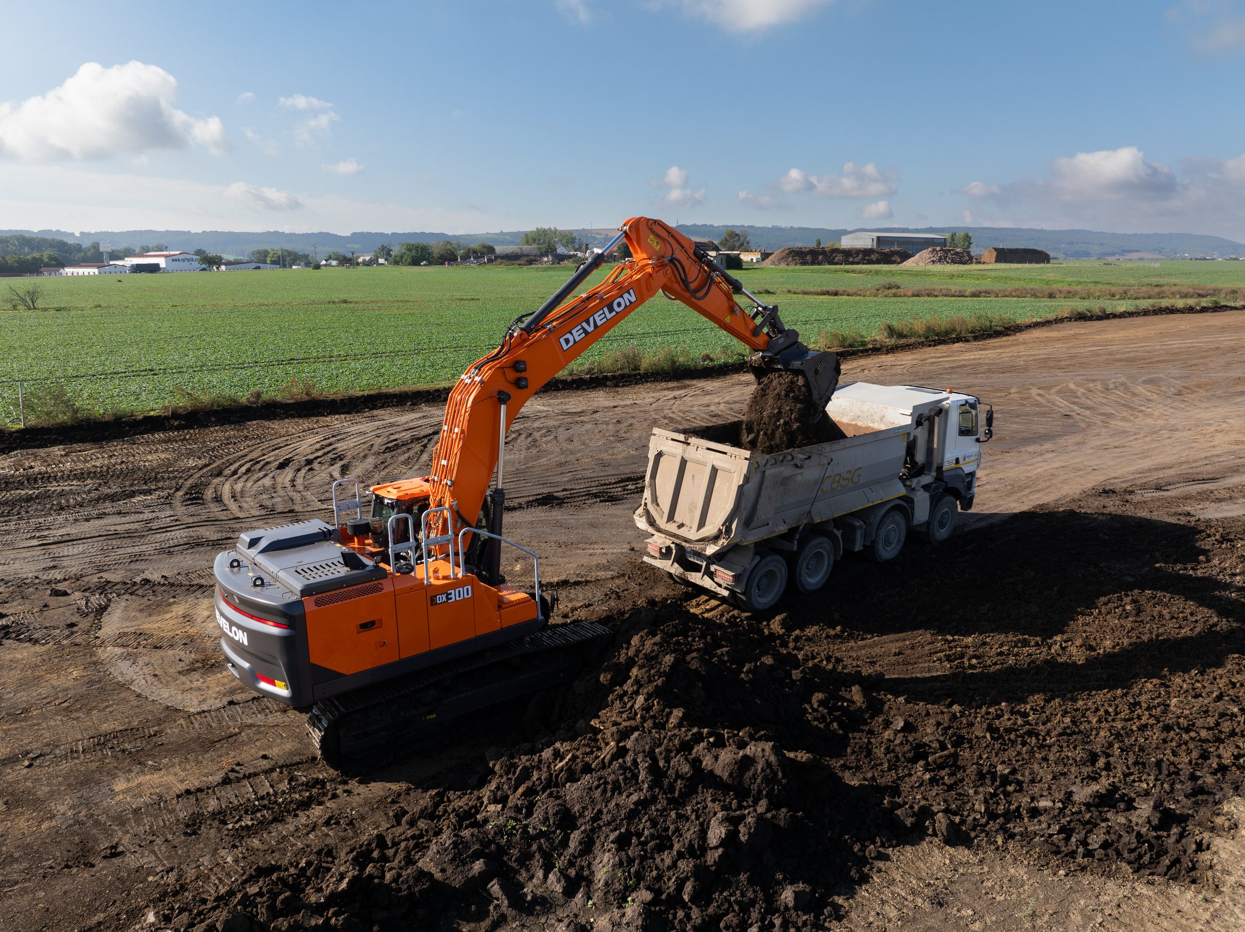 L'escavatore cingolato DEVELON DX300LC-9 da 32 tonnellate all'opera in cantiere mentre carica un dumper, mostrando la sua elevata produttività nelle attività di movimento terra.