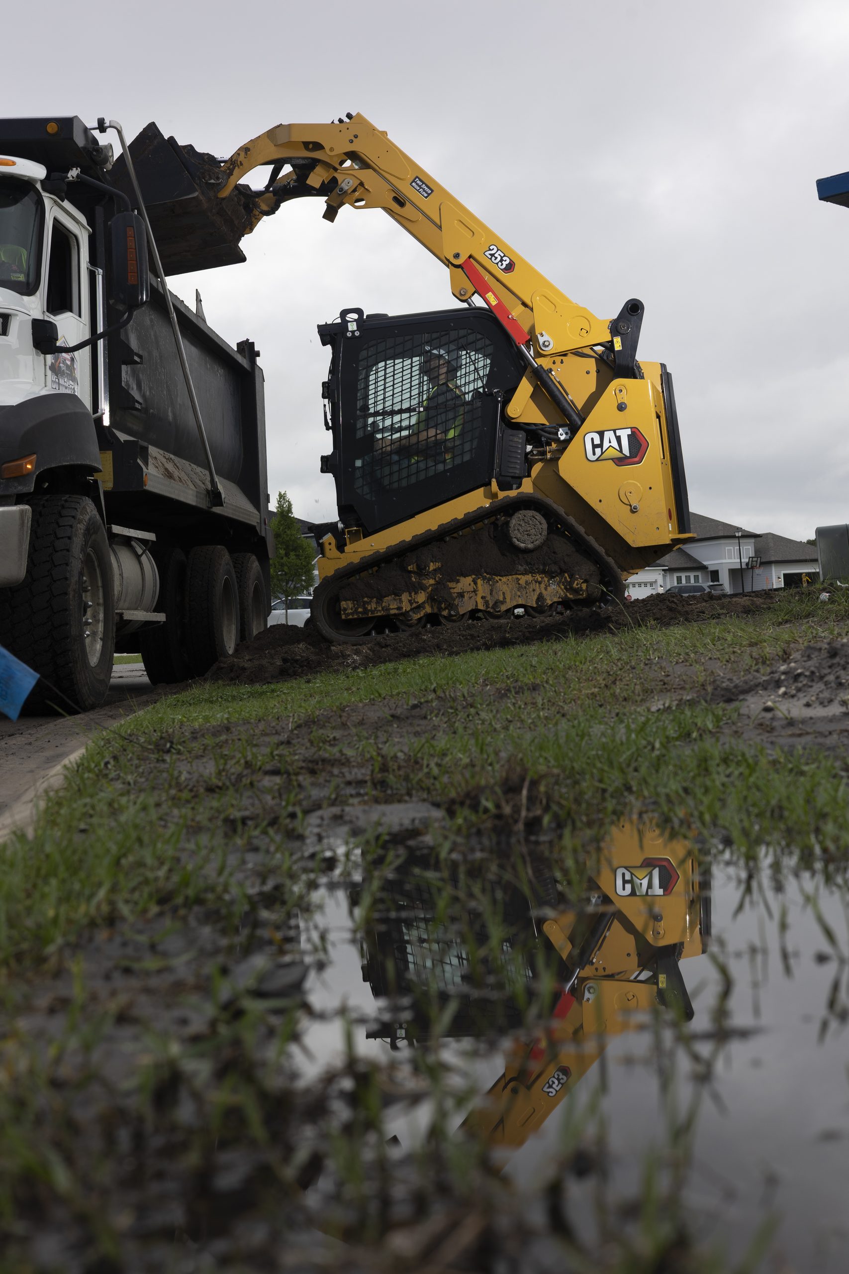 Il nuovo caricatore cingolato compatto Caterpillar Cat® 253 all'opera in cantiere durante le operazioni di carico, evidenziando le prestazioni del sottocarro monoblocco e la versatilità nella movimentazione dei materiali.