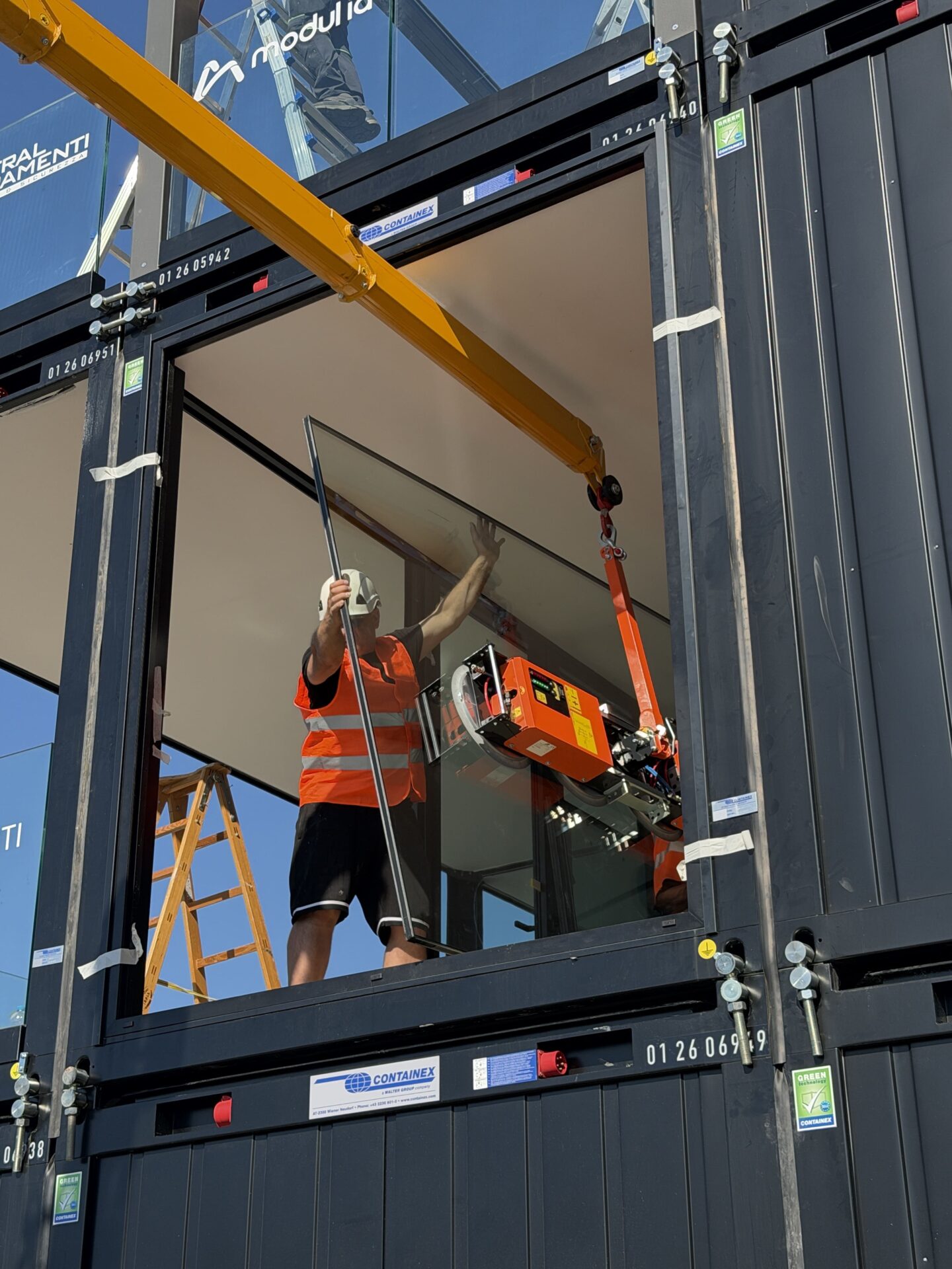 Operai al lavoro con la minigru Jekko SPX532.2 e la ventosa per l'installazione dei pannelli in vetro all'interno dei container del Villaggio Barcolana a Trieste.